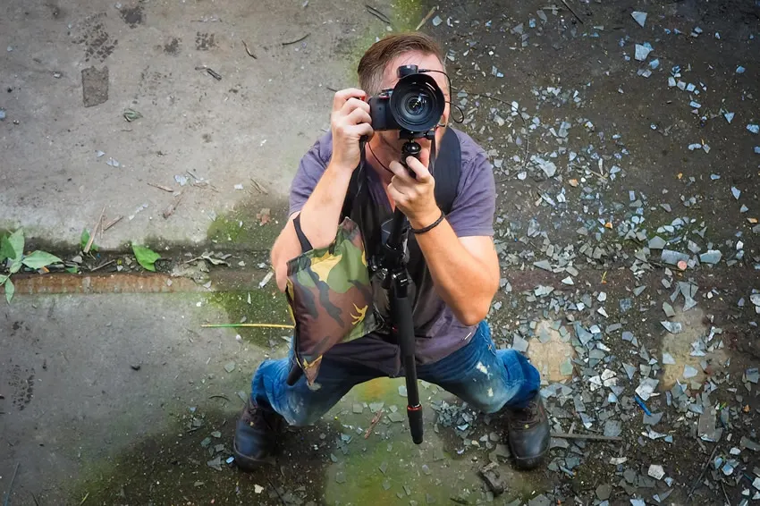 A photographer crouching in challenging conditions shooting upward with a camera on a monopod